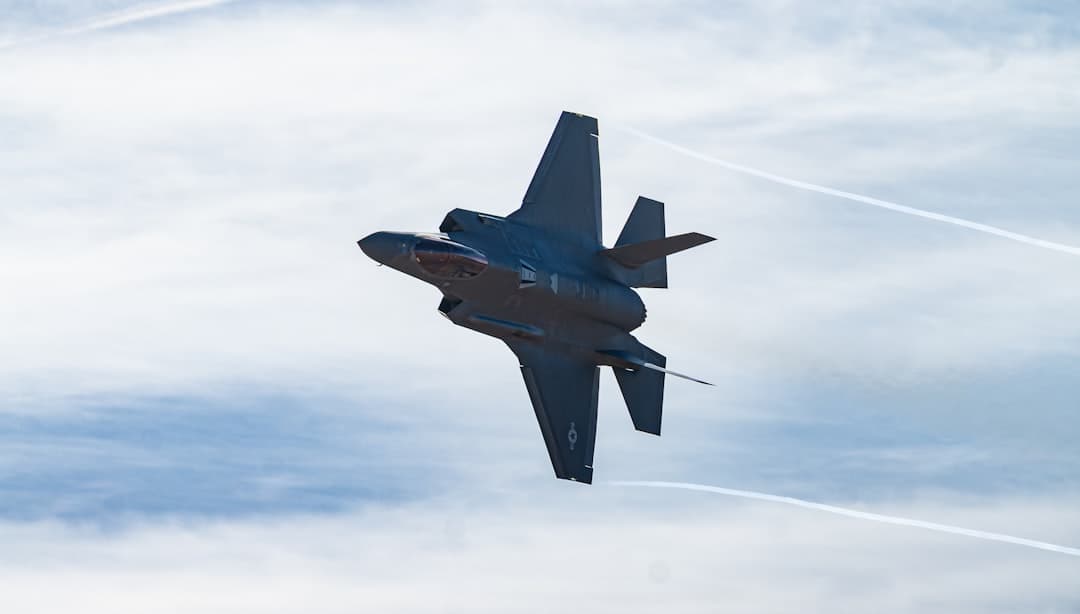 A dark fighter jet performs a maneuver in the sky.